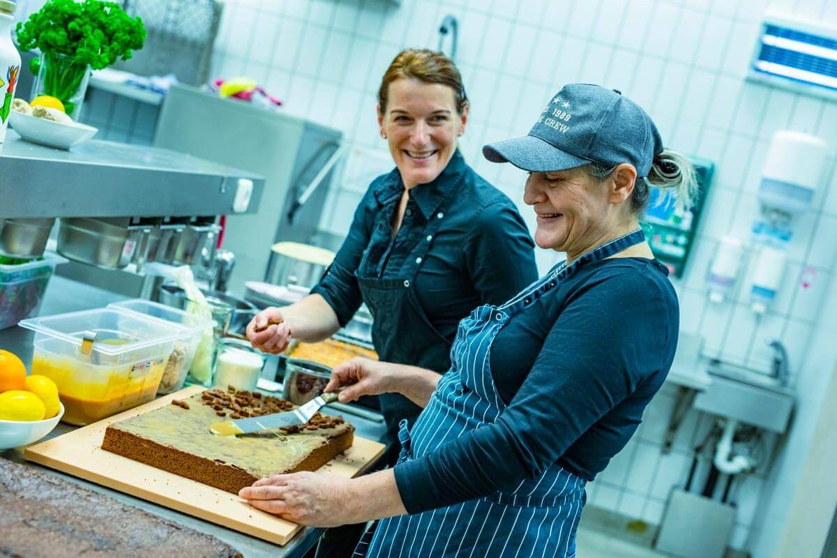 In der Küche des Bauchladen backen zwei Mitarbeiterinnen ein Schokokuchen.