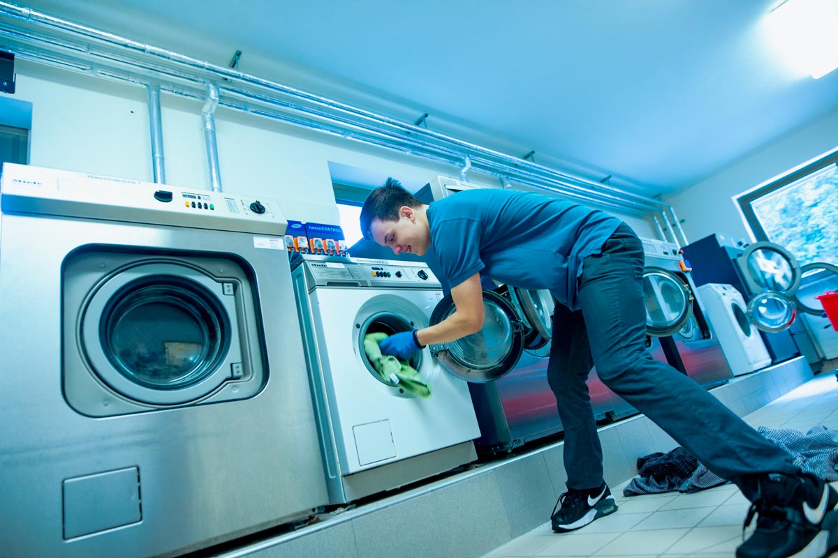 Die großen Gewerbewaschmaschinen im Textil- und Reinigungsservice werden von einem Auszubildenden mit Wäsche befüllt