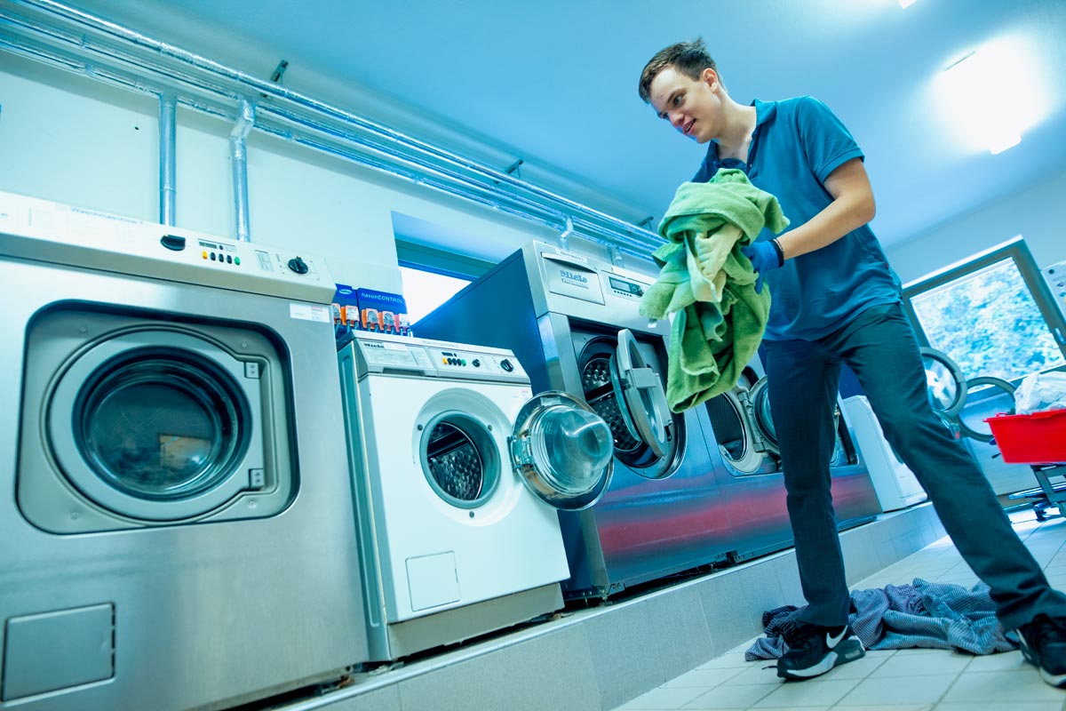 Die großen Gewerbewaschmaschinen im Textil- und Reinigungsservice werden von einem Auszubildenden mit Wäsche befüllt