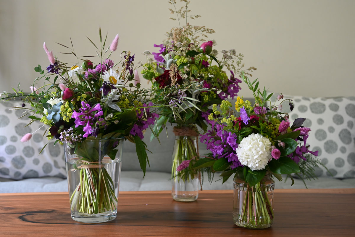 Auf einem Tisch stehen drei Blumensträuße in verschiedenen Größen aus selbstgezogenen Gartenblumen.
