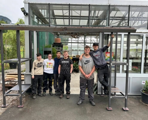 Jugendliche aus der Schlosserei stehen unter dem neuen Glashaus-Vordach am Campus von oberrainanderskompetent