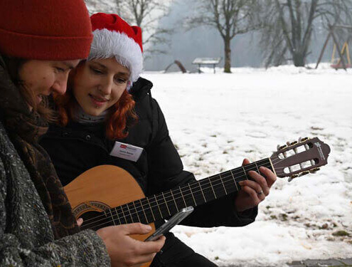 Zwei Frauen mit Gitarre und Handy im verschneiten Park, Inklusion beim Weihnachtsmarkt Salzburg