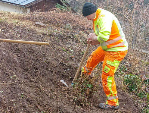 Person in Warnkleidung gräbt auf einer Böschung ein Pflanzloch für eine Aufforstungsaktion