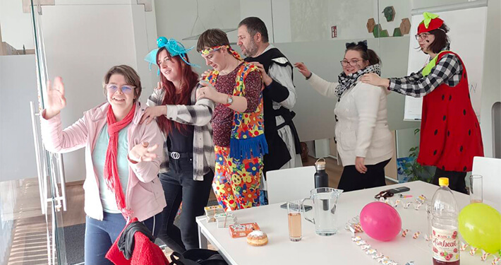 Verkleidete Menschen feiern lachend Fasching, bunte Deko auf Tisch, gelebte Inklusion Saalfelden