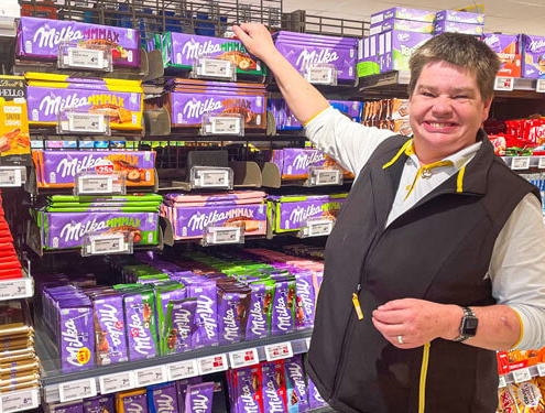 Mitarbeiter mit Behinderung präsentiert Schokoladenregal bei Arbeitsintegration im Sozialunternehmen