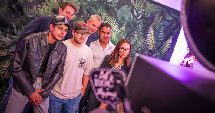 Gruppe junger Menschen posiert vor Fotobox mit Pflanzenhintergrund