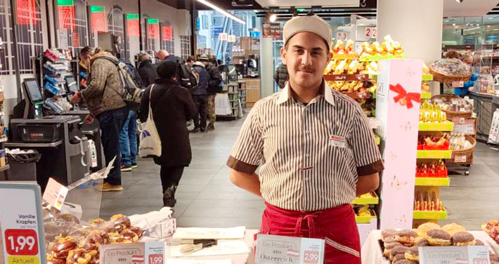 Verkäufer in Marktfiliale steht hinter einem Gebäckstand