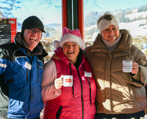 Drei Personen an einem Wintermarktstand lächeln und halten Becher