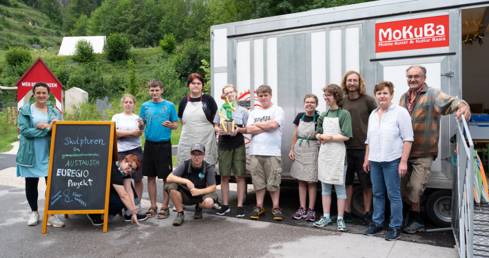 Gruppe mit Kunstobjekten vor dem MoKuBa-Container, daneben eine Tafel zum EUREGIO-Projekt